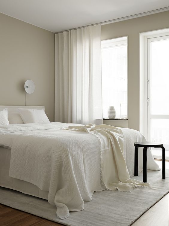 a serene bedroom with greige walls, creamy and black furniture, creamy bedding and curtains plus lots of natural light incoming