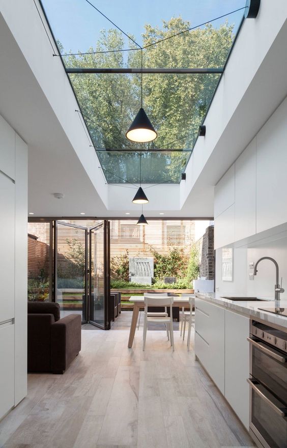a slee minimalist kitchen in white with a glazed folding wall and a large skylight that lights up the kitchen