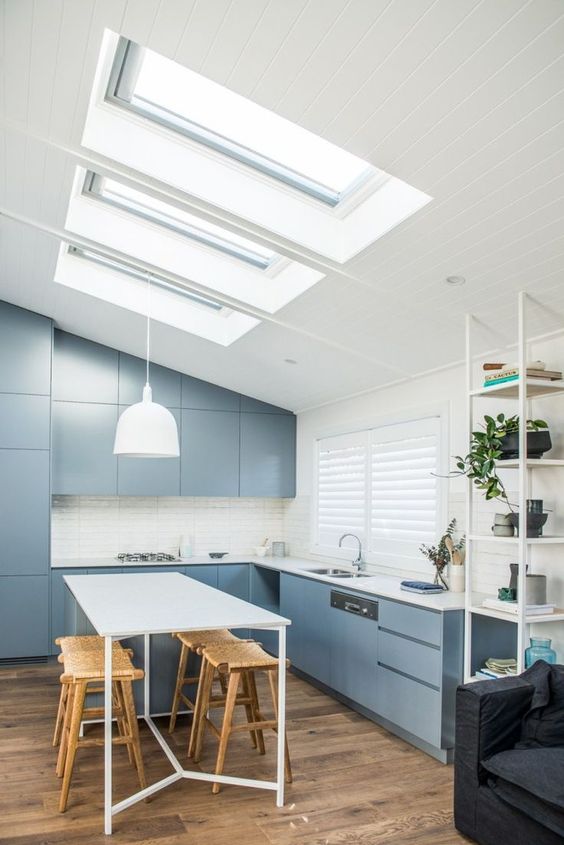 a sleek and plain blue ktichen with white countertops and a white backsplash, a series of skylights that illuminates the space