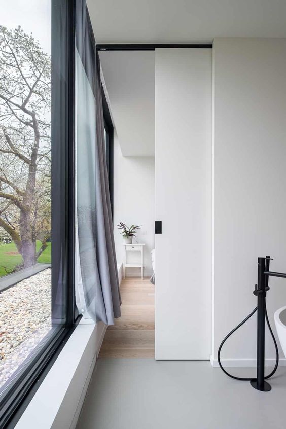 a small and delicate white pocket door with a black handle is a cool idea to hide a bathroom in a bedroom and looks cool