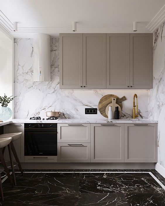 a small contemporary greige kitchen with shaker cabinets, a white marble backsplash and countertops and built-in appliances is wow