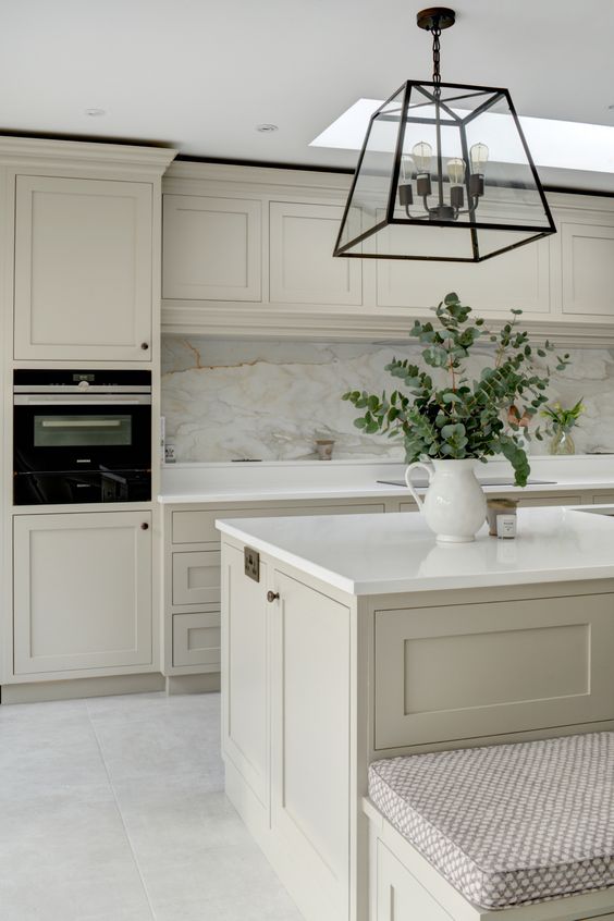 a stunning greige kitchen with shaker cabinets, a large kitchen island, a marble backsplash and white stone countertop plus a pendant lamp