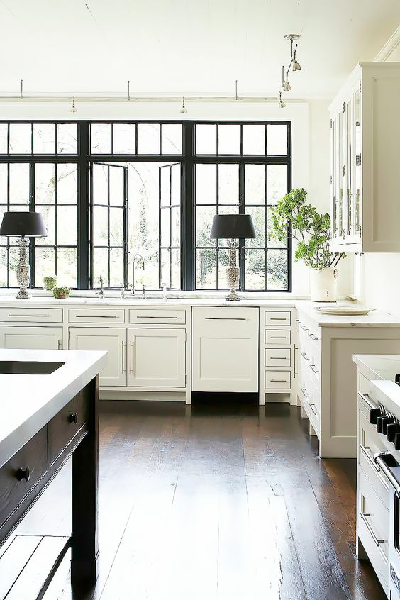 a stylish and elegant kitchen in white and black, with black painted French windows, black table lamps, a dark kitchen island and potted plants