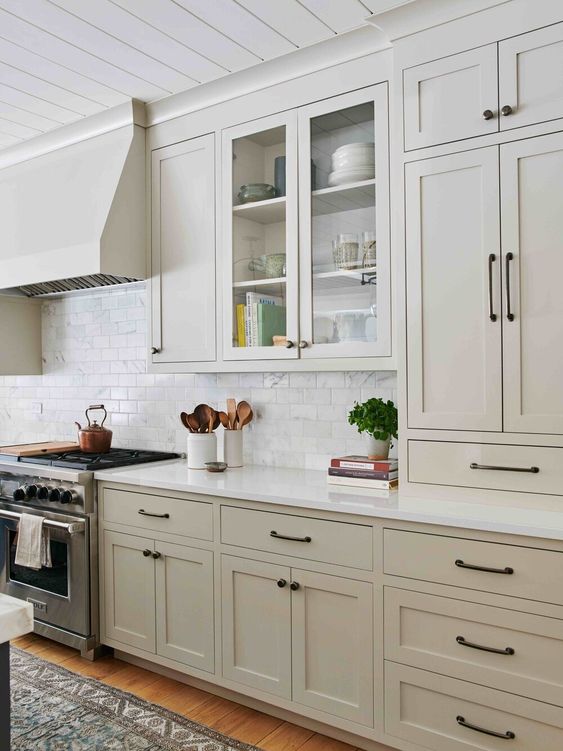 a stylish greige kitchen with white stone countertops, a white subway tile backsplash and black fixtures is chic and cool