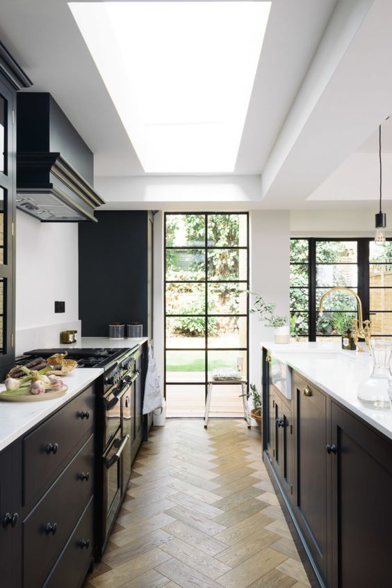 a stylish modern black kitchen with a large skylight and French windows with black frames, a black hood and a parquet floor