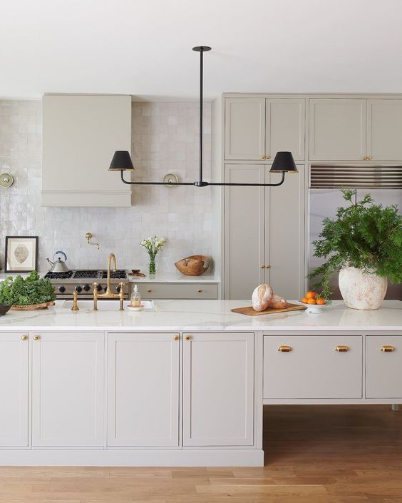 a subtle greige kitchen with shaker cabinets, a catchy kitchen island, a black chandelier, a glossy tile backsplash and white stone countertops