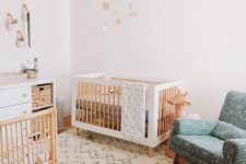 a welcoming Scandi nursery with white and stained furniture, a blue rocker chair, jute poufs, a white dresser and a pendant lamp