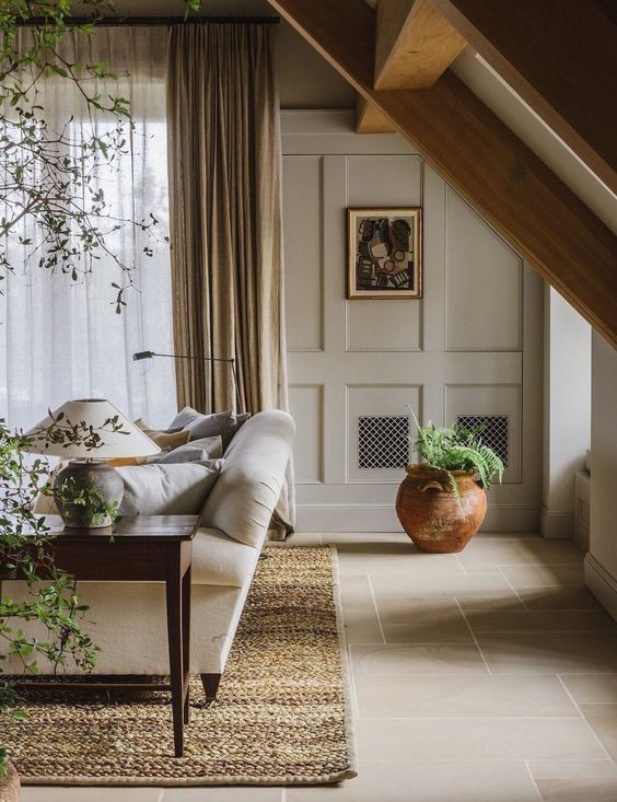 a welcoming greige living room with paneled walls, a neutral sofa, a dark stained coffee table, potted plants and a warm-colored rug