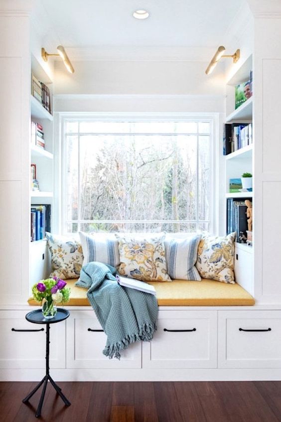 a window with a built-in storage unit with a seat, with built-in shelves and lots of pillows and a blanket is a lovely nook to read something