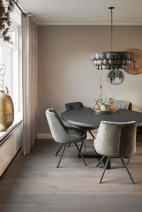 an elegant and refined greige dining room with a black round table, grey chairs, a black metal chandelier, decorative plates and a candle