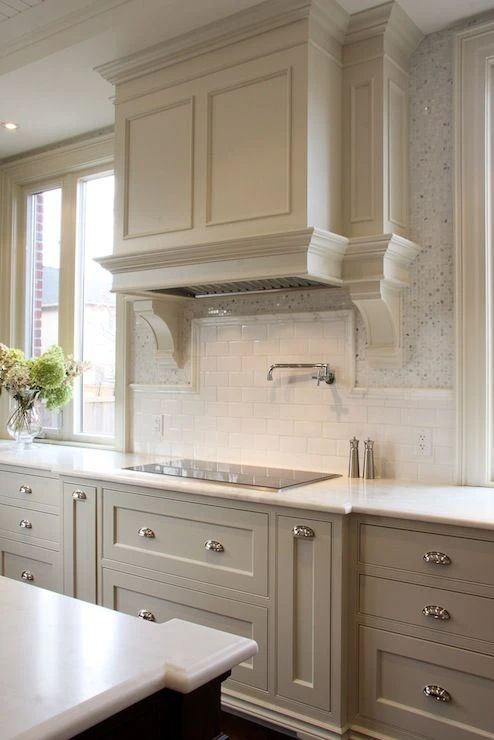 an elegant vintage farmhouse kitchen with shaker cabinets, a large matching hood, a white subway tile backsplash and white stone countertops is chic