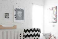 an inviting Scandi nursery with wallpaper walls, a white and stained crib, a rocker, a grey rug and some monochromatic bedding