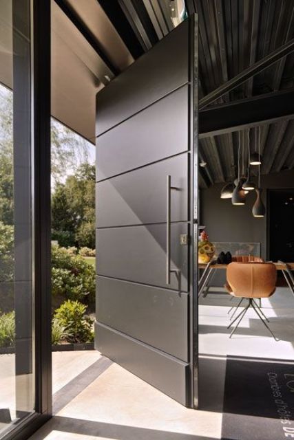 an oversized blackened metal front door with a usual handle is a cool idea for a modern home and can fit soem other styles, too
