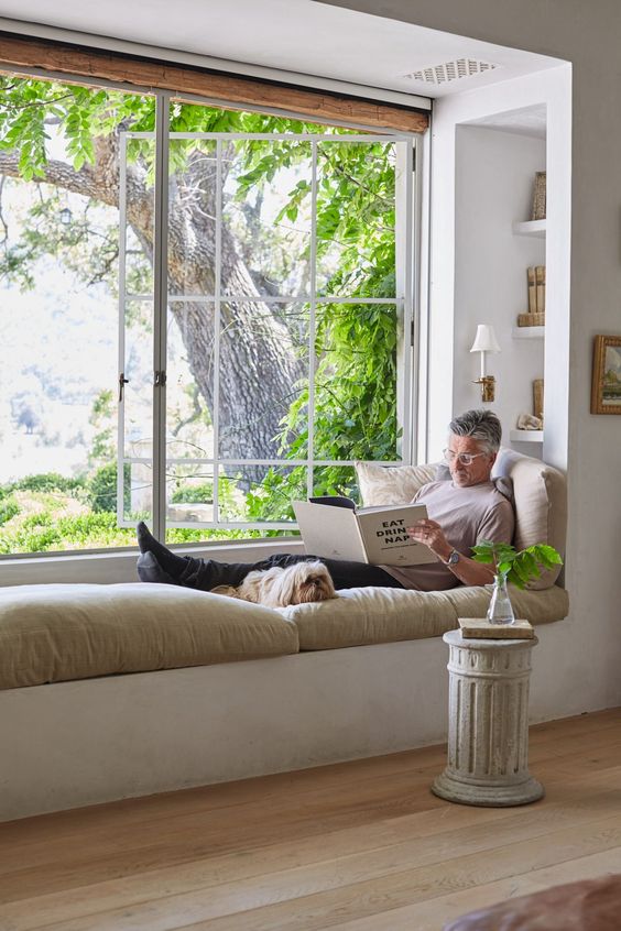 an oversized window with built-in shelves, a daybed and fost and cool pillows and cushions is an ultimate nook to spend time in