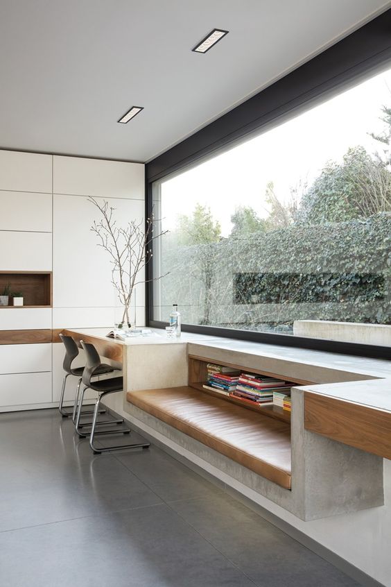 an oversized panoramic window with a concrete windowsill, a built-in table, a seat with a leather cushion and a niche for book storage