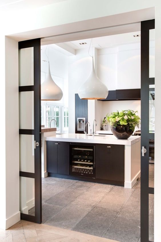 a stylish contemporary kitchen in black and white, with black French pocket doors that match the decor and separate the spaces