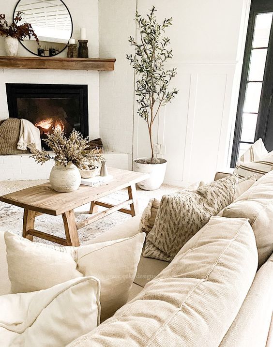 a neutral living room with super natural decor, a mantel, potted plants, a wooden coffee table and lots of pretty pillows