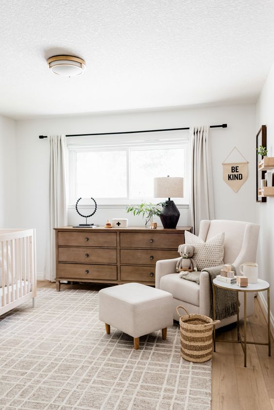 a mid-century modern neutral nursery with a white crib, a neutral chair with a footrest, a stained dresser and neutral textiles is welcoming
