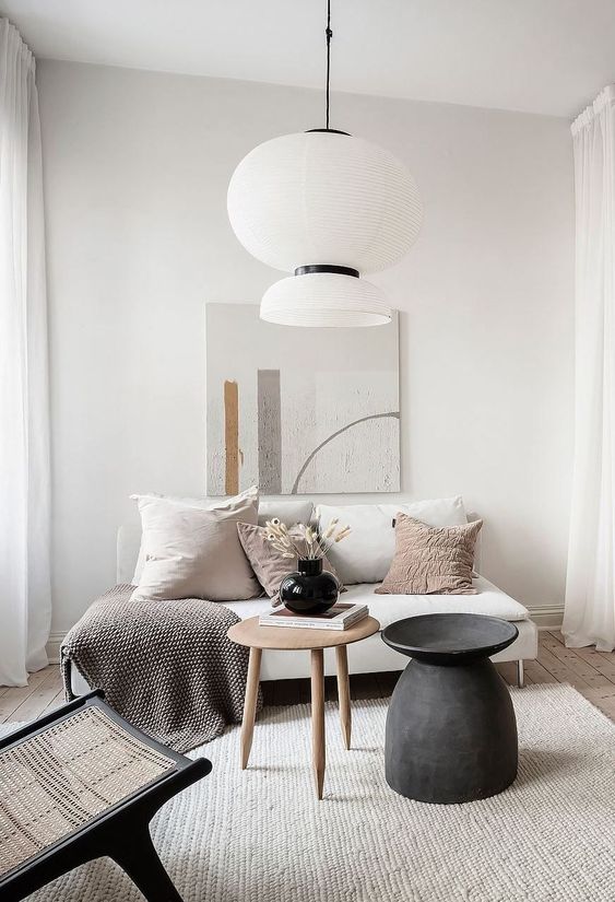 a small yet minimal living room with a neutral loveseat, a couple of coffee tables, a cool artwork and a woven chair