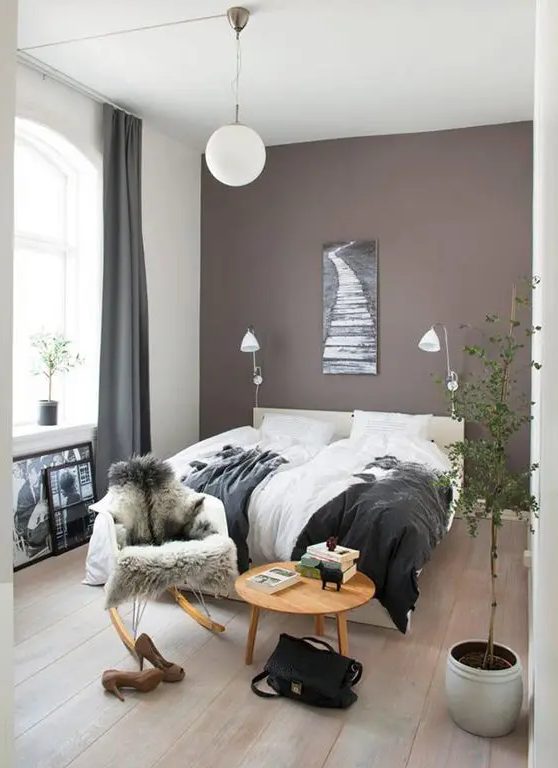 a beautiful boho bedroom with a taupe accent wall, a creamy upholstered bed and lovely bedding, a round table and a chair, a potted plant