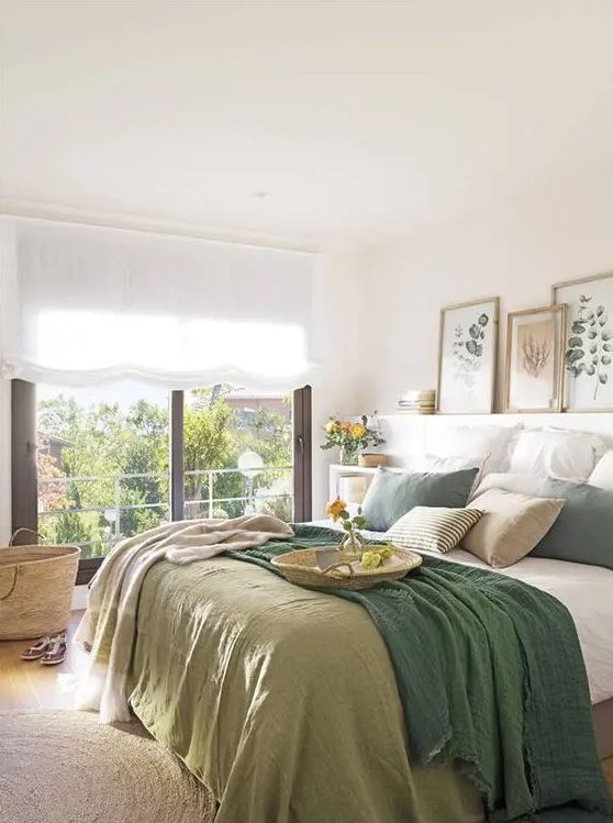 a modern country bedroom with natural touches, a ledge with artworks, a bed with green and white bedding and a large window