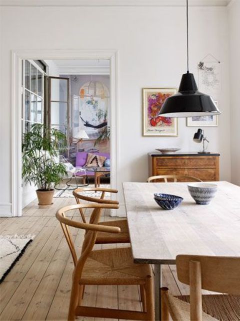 a Nordic dining space with a rich-stained buffet, a light-stained table and warm-stained chairs, black pendant lamps