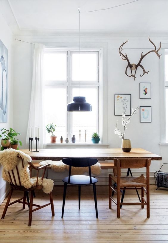 a Scandi dining space with a light stained floor, a rich stained table and chairs, black chairs and some potted plants is amazing