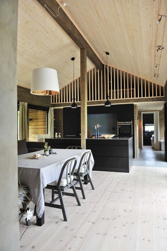 a Scandinavian kitchen with black cabinetry and a kitchen island, a whitewashed floor, a black table and chairs plus a light-stained ceiling