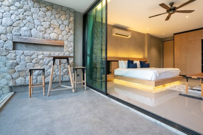 a beautiful space with a stone accent wall, glass sliding doors and a floating lit up bed with cool bedding is wow
