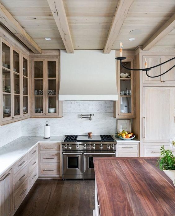 a catchy and welcoming kitchen with a whitewashed ceiling and cabinets, with a reclaimed wood floor and a kitchen island with a reddish countertop