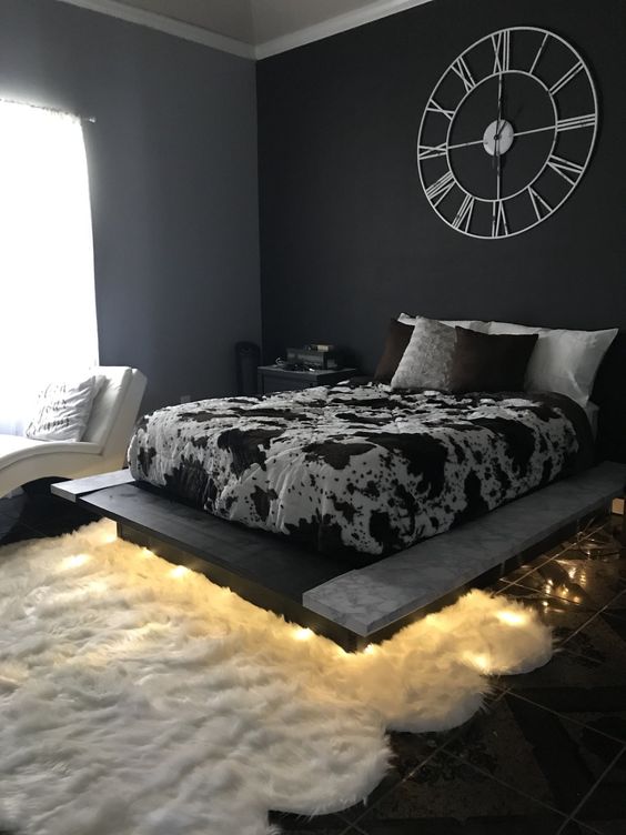 a catchy bedroom with grey and an accent black wall, a floating bed with lights, a white curved couch and printed bedding