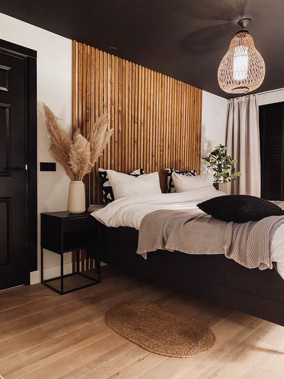 a chic and contrasting bedroom with a black ceiling, a wooden plank accent, a black floating bed and cool nightstands, a woven lamp and black and white bedding