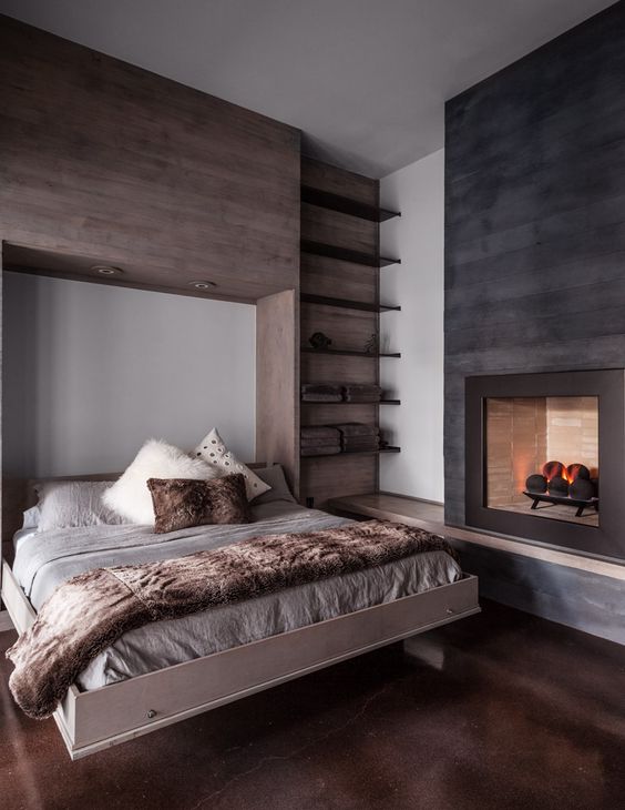 a cozy modern chalet bedroom with a floating bed, floating shelves, a fireplace and some faux fur bedding is very welcoming