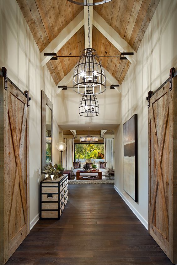 a farmhouse space with a dark-stained wooden floor, a light-stained ceiling and sliding doors plus elegant furniture, art and pendant lamps