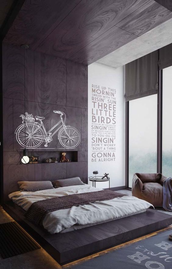 a gorgeous bachelor bedroom with a dark floating platform bed and a headboard extended to the ceiling, a leather chair and a letter accent on the wall