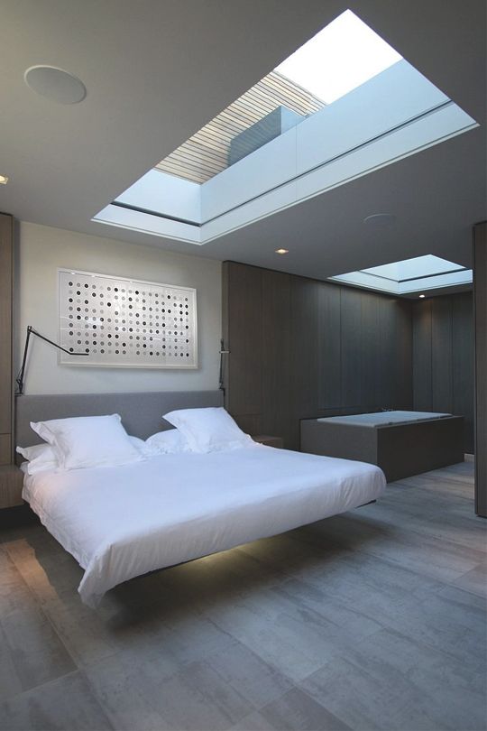 a minimalist bedroom with a large skylight, a floating lit up bed, a bathtub clad with wooden panels is a chic space