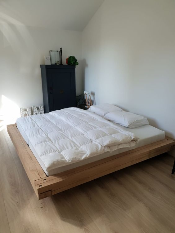 a modern and laconic bedroom with a light-stained floating bed, a black storage unit, some marquee letters and neutral bedding