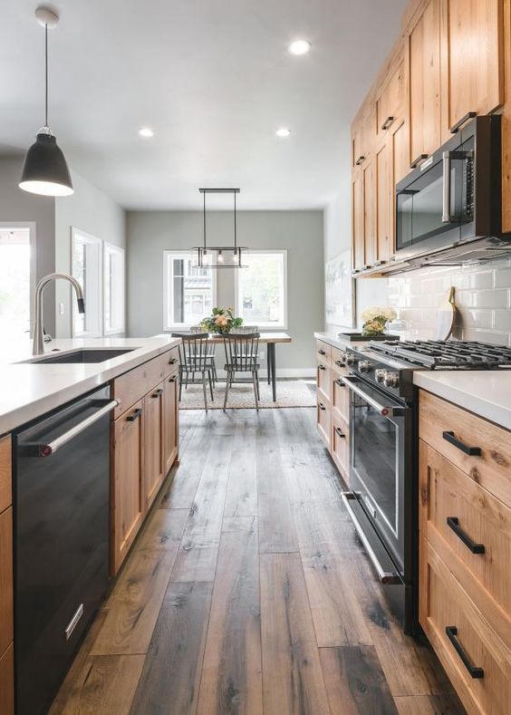 a modern farmhouse kitchen with light stained cabinets, black built in appliances and a dark reclaimed wood floor is amazing