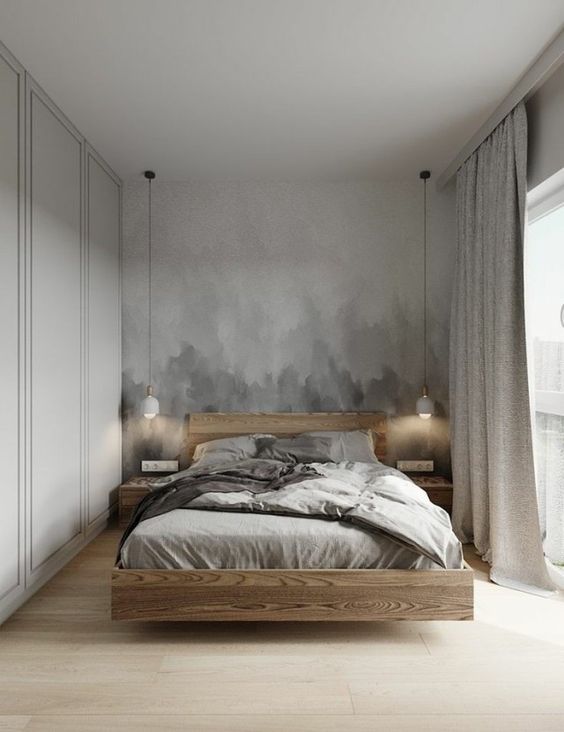 a neutral bedroom with a grey ombre accent wall, a floating light-stained bed and nightstands, pendant lamps and grey bedding