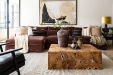 a refined living room with a burgundy sectional, a black chair, a light-stained wooden floor, a neutral rug and a rich-stained wooden table