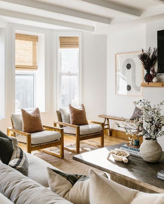 a sophisticated neutral living room with a large sofa, white chairs with warm-stained wood, a reclaimed wood coffee table for a contrast