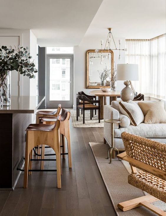 a stylish light filled open layout with a welcoming bar space, living room and a dining zone, with varioys neutral wood tones and a dark wood floor and kitchen island