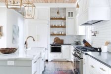 a white farmhouse kitchen with a light-stained planked ceiling, a reclaimed wood floor, white cabinets and elegant gold pendant lamps