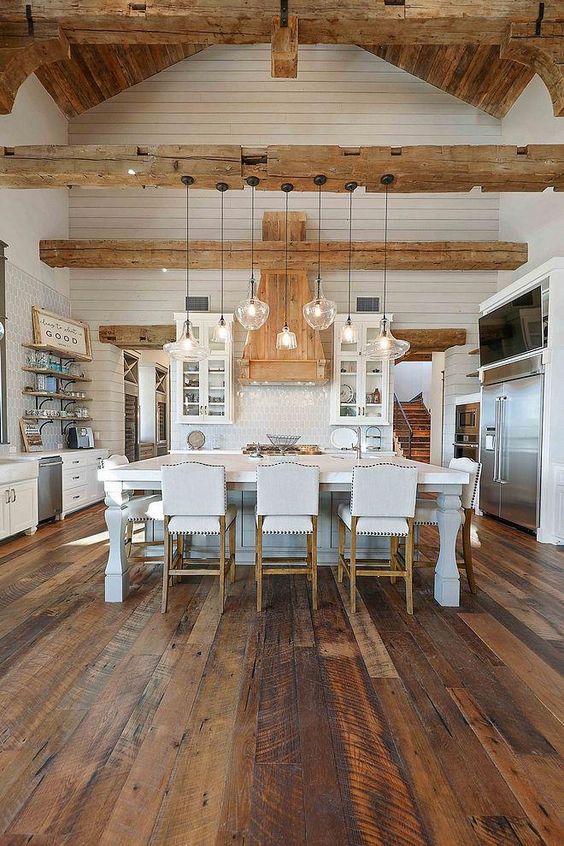 a white farmhouse kitchen with white cabinets, a refined kitchen island, a reclaimed wooden floor, light-stained wooden beams and a ceiling
