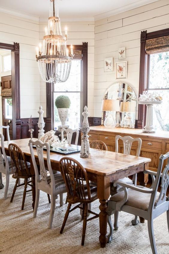 an eclectic dining room with dark-stained panels, a light-stained buffet, a rich-stained table and mismatching chairs plus a crystal chandelier