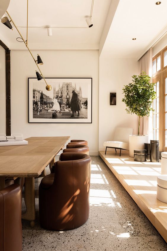 an exquisite space with a grey terrazzo floor, a light-stained platform by the window, a warm light-stained table and chocolate leather chairs