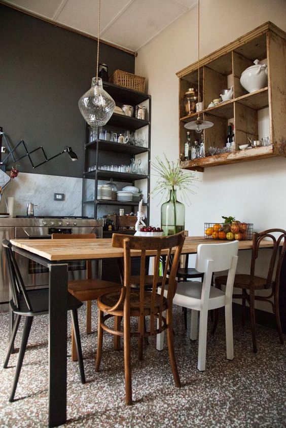 an industrial kitchen with a marble backsplash, a light-stained box shelf, a light-stained table and mismatching chairs plus pendant lamps