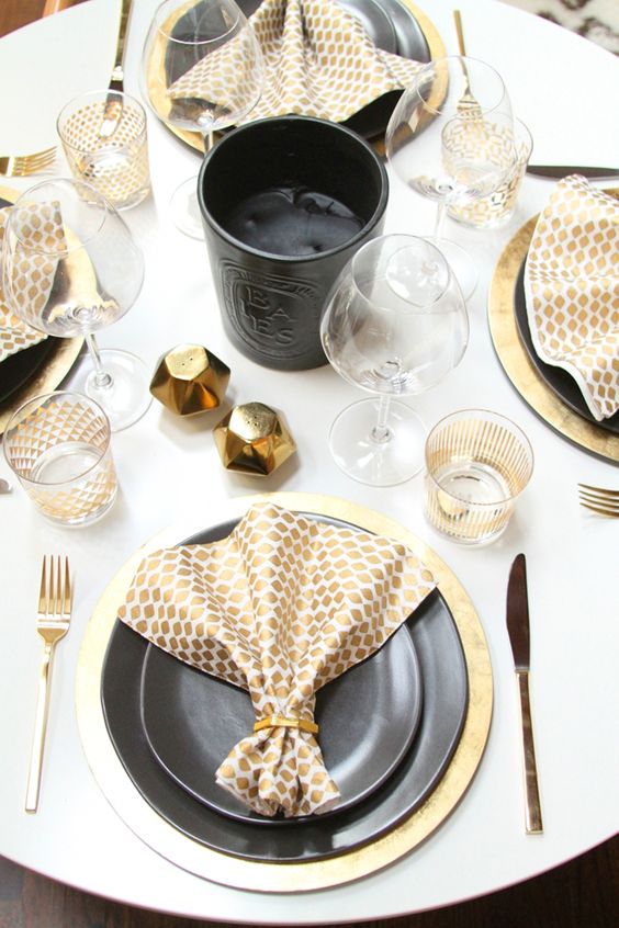 a beautiful black and gold Thanksgiving tablescape with gold pinted napkins, chargers, cutlery and spice containers, a black candle in the center and plates