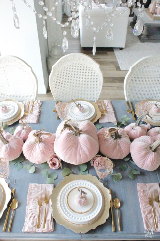 a chic and beautiful Thanksgiving tablescape with a grye tablecloth, pink velvet pumpkins and napkins, gold chargers and cutlery plus greenery