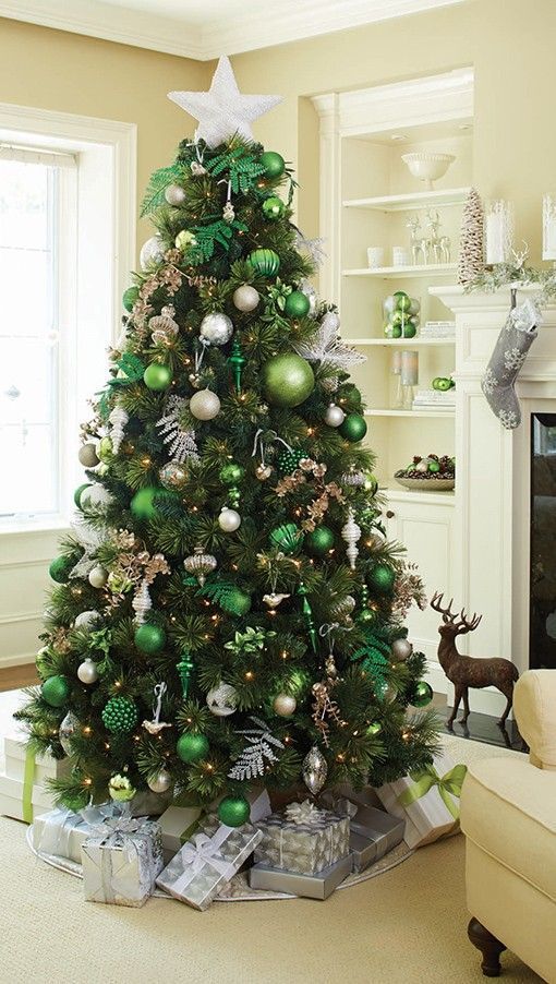 a beautiful forest glam Christmas tree with lots of green and white ornaments of various sizes, silver leaves, lights and branches plus a white star on top